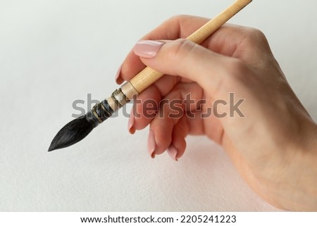 A woman paints with a brush. A woman's hand holds a brush. Watercolor painting. Learning to draw with paints. Elegant female hand with a brush.. Watercolor brush in a female hand.