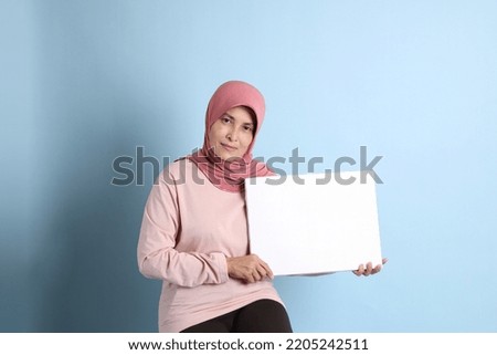 The senior southeast Asian woman with hijab sitting on the blue background