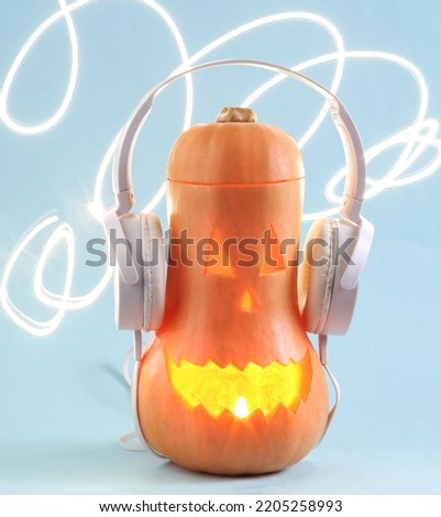 Glowing Halloween pumpkin with stereo headphones on blue bright background. Scary glowing face, sinister smile. Minimal halloween or music concept. Trick or Treat