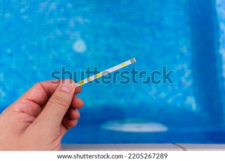 Hand with measuring pool strips to check water quality in a swimming pool Royalty-Free Stock Photo #2205267289
