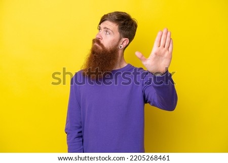 Redhead man with beard isolated on yellow background making stop gesture and disappointed