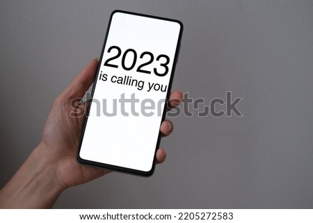 2023 Is Calling You. Happy New Year 2023 concept with hand holding a smartphone. High resolution photo for large displays, print, website banners, social media communication posts.