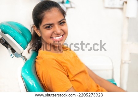 Side view images of beautiful young Indian female patient sitting on a chair at dentist clinic. She happily smiles for the camera after successful detail treatment. Royalty-Free Stock Photo #2205273923