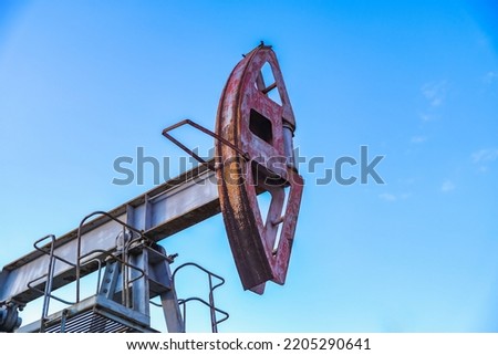 An abandoned oil or gas rocking machine against a blue sky, exhausted resource. A clogged field of gas and oil production.