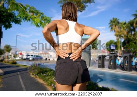 Athletic woman on running track touching hurt back with painful injury. High quality photo