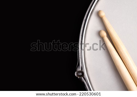 Snare drum with coated head and drumstick on black background with big copy space for text. 
