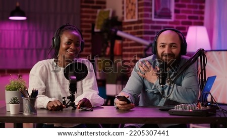 Diverse team of online radio hosts recording podcast review for smartphone streaming audio with digital mixer. Content creator and african american influencer broadcasting live product presentation.