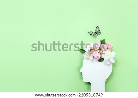Cardboard silhouette of human head decorated with flowers and butterfly on green background. World mental health day concept. Copy space