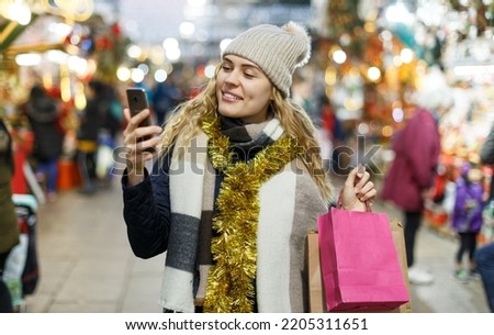 Cheerful young woman making picture on her smartphone at Christmas fair