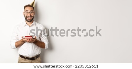 Holidays and celebration. Happy man having birthday party, making wish on b-day cake and smiling, standing against white background