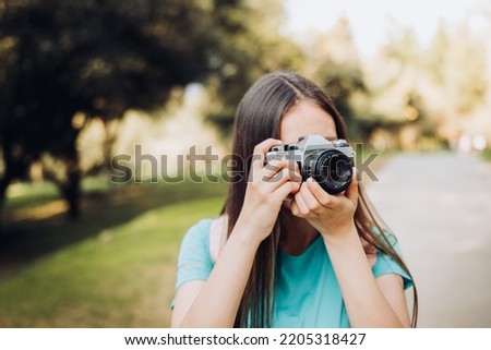 Young tourist girl, taking photos with a vintage film camera while walking in the park.