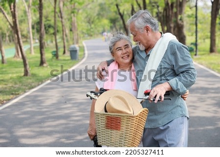 Portrait of happy asian senior man and woman walking and hugging with bicycle and binoculars in summer garden outdoor. Lover couple going to picnic at the park. Happiness marriage lifestyle concept.