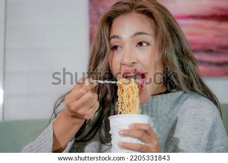 Asian woman enjoy eating hot instant noodles alone in the living room after house work. Young Freelance female work from home.