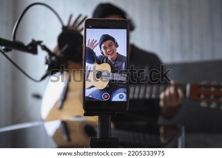 Asian influencer playing guitar during podcast or live video broadcast for the audience from the mobile phone at home Royalty-Free Stock Photo #2205333975
