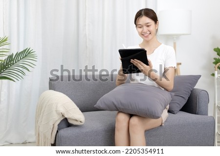 Asian woman sitting on the sofa with a tablet, Looking at tablet screen, Relaxing at home, Weekend activities, Comfort Zone, Happy working lifestyle, Happy lifestyle, Feel good.
