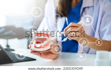 Concentrated dentist sitting at table with jaw samples tooth model and working with tablet and laptop in dental office professional dental clinic. with VR icon
