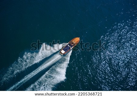 Luxurious wooden motor boat rushes through the waves of the blue Sea. Classic Italian wooden boat fast moving aerial view. Luxurious wooden boat fast movement on dark water. Royalty-Free Stock Photo #2205368721