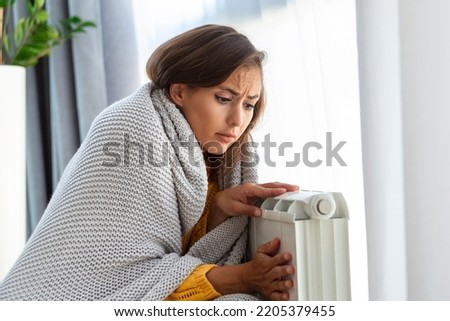 Woman freezing at home, sitting by the cold radiator. Woman with home heating problem feeling cold