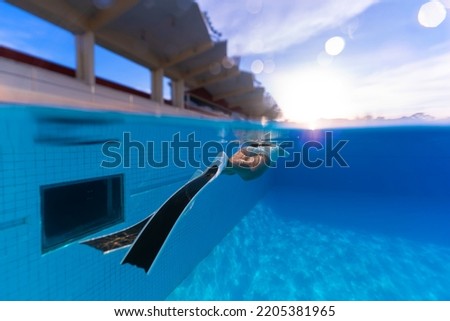 Underwater photography of water sports of a young woman wearing a swimsuit. Practice dynamic freediving in the clear blue outdoor swimming pool. Learn to dive on vacation, focus on the fin. Royalty-Free Stock Photo #2205381965