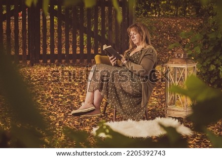 Vintage style autumn mood picture of a woman enjoying reading a book in a fairy garden with colorful leaves