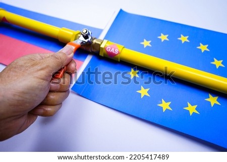 Man's hand​ holding gas pipe value on Russian and European flags, Russian closes gas pipeline to Europe. 