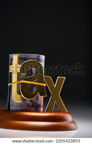 Judge's gavel with dollars in roll with single word tax  against gray background Royalty-Free Stock Photo #2205423893