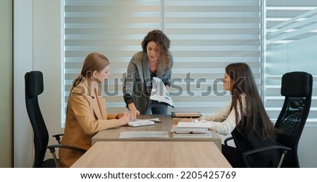 Three females working on financial business goal showed on paper report in office. Team exchanging papers and ideas on current client case. Royalty-Free Stock Photo #2205425769