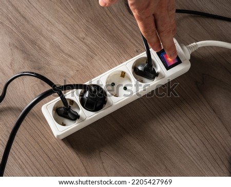 A man cutting off the electrical current by turning off the button on a white electrical socket to reduce energy consumption Royalty-Free Stock Photo #2205427969