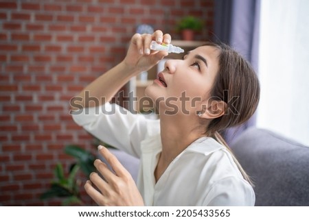 Young asian woman using medical eyes drops suffering from dry eyes syndrome or curing ophthalmology disease at home. Blurred eyesight, Treating eyes. Royalty-Free Stock Photo #2205433565