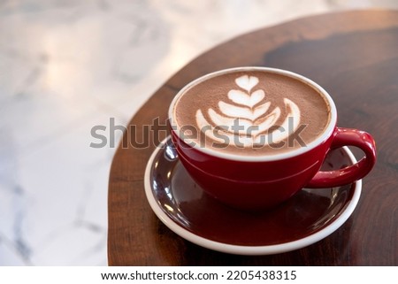 Freshly served cup of hot chocolate with beautiful latte art on a wooden table in a cafe.
