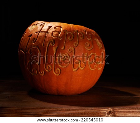 Pumpkin with the words Happy Halloween carved on its surface, placed over the wooden boards in a low key lighting composition