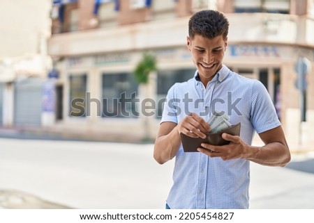 Young hispanic man smiling confident holding wallet with dollars at street Royalty-Free Stock Photo #2205454827