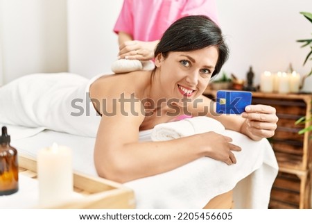 Middle age hispanic woman holding credit card having back massage using thai bags at beauty center