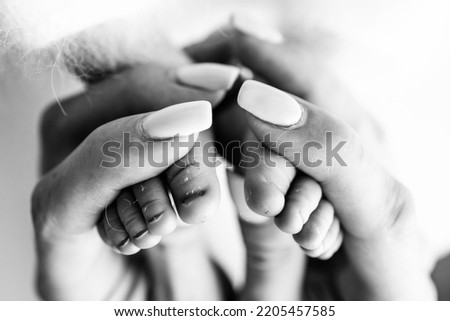 The palms of the parents. A mother hold a newborn baby by the legs. The feet of a newborn in the hands of parents. Photo of foot, heels and fingers. Black and white studio macro photography