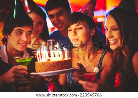 Charming female blowing on candles on birthday cake after making her wish at party
