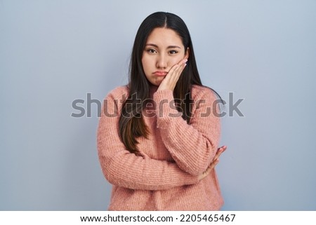 Young latin woman standing over blue background thinking looking tired and bored with depression problems with crossed arms. 