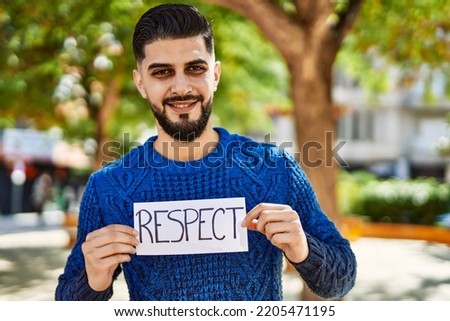 Young arab man smiling confident holding respect banner at park