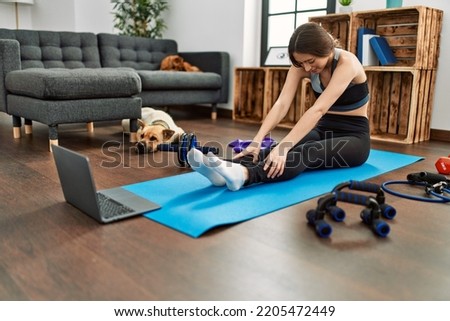 Young hispanic woman having online stretching class at home