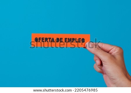 a man is holding an orange paper sign with the text job offer written in spanish, against a blue background Royalty-Free Stock Photo #2205476985