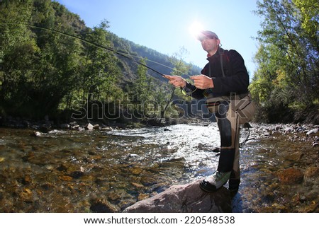 Fly fisherman using flyfishing rod in beautiful river  Royalty-Free Stock Photo #220548538