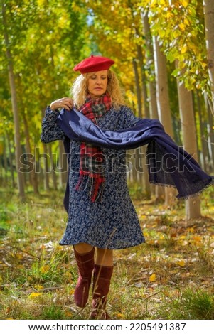 a woman and model carries in her hands a large scarf walking through the forest full of leaves and trees in autumn