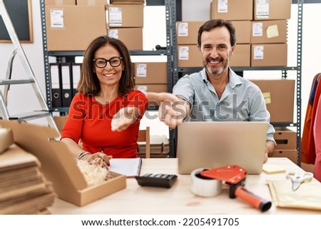 Middle age couple working at small business ecommerce smiling cheerful offering palm hand giving assistance and acceptance. 