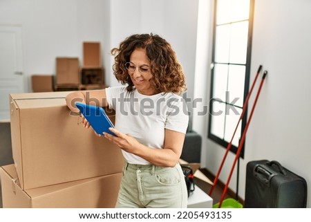 Middle age hispanic woman smiling confident using touchpad at new home