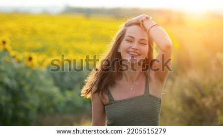 Woman wearing green dress runs past blooming sunflower field. Brown-haired lady enjoys life looking with smiling expression against blurry countryside