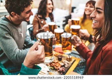 Happy friends enjoying happy hour drinking beer at brewery pub - Group of young people hanging out dining together at bar restaurant - Beverage lifestyle and friendship concept