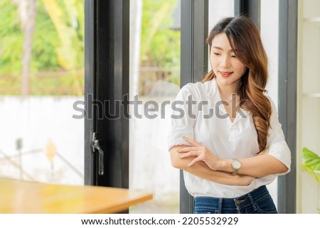 Smiling Asian woman standing with her arms crossed looking at the camera at work
confidently
