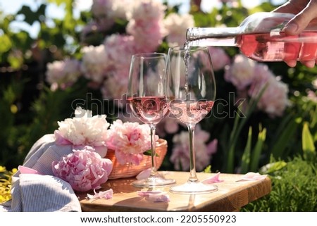 Woman pouring rose wine into glass at table in garden, closeup