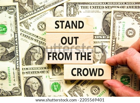 Stand out from the crowd symbol. Concept words Stand out from the crowd on wooden blocks on beautiful background from dollar bills. Businessman hand. Business, stand out from the crowd concept