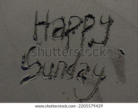 Close up. The word Happy Sunday written in sand beach with wave in background. Outdoor picture in summer season. Day, weekend, travel and relaxation concepts.