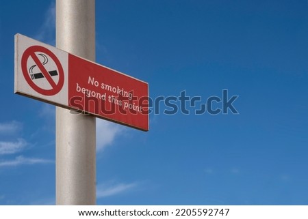 Warning sign icon on a pole with text "no smoking beyond this area" against a blue sky
